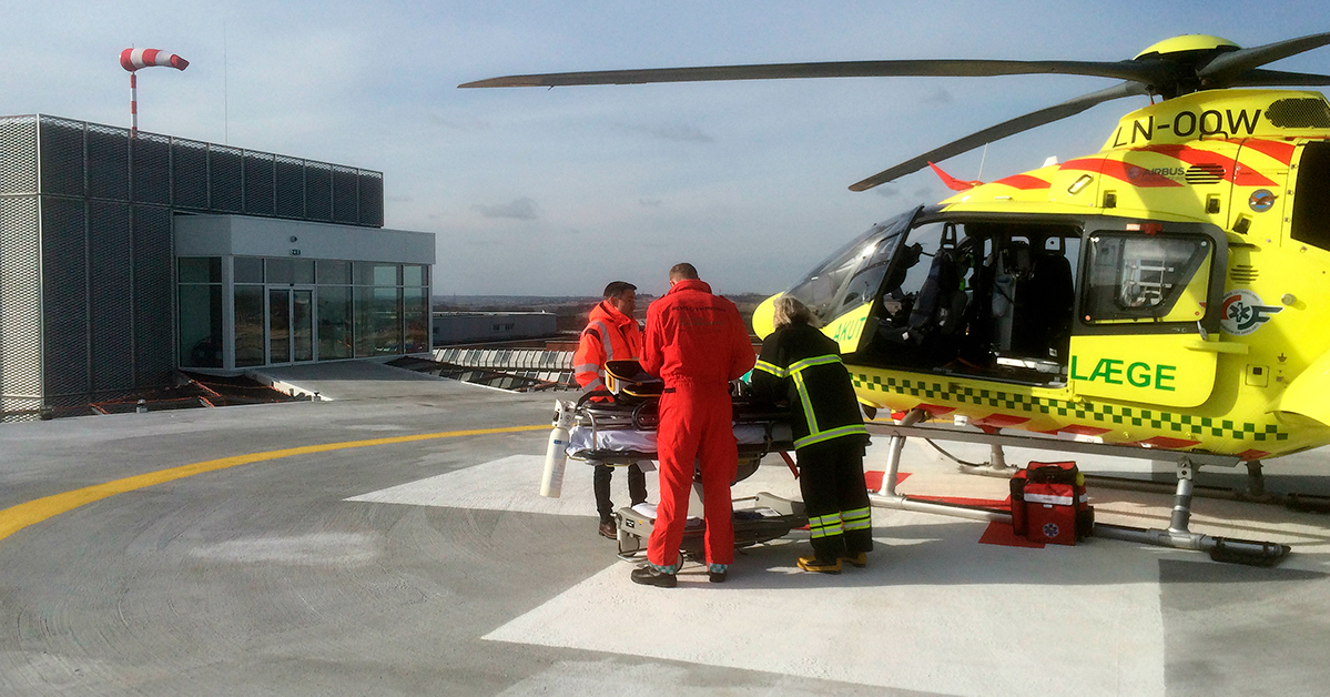 3 helikopterreddere fører en skadet person ud af redningshelikopteren der er landet på hospitalet